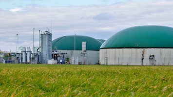 Biogas plant with green domed digesters beside a rural grass field