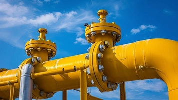 Yellow gas pipes with bolted flanges and valve assemblies against a blue sky