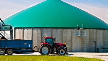 Red tractor with blue trailer at a large anaerobic digestion facility beneath a distinctive green dome